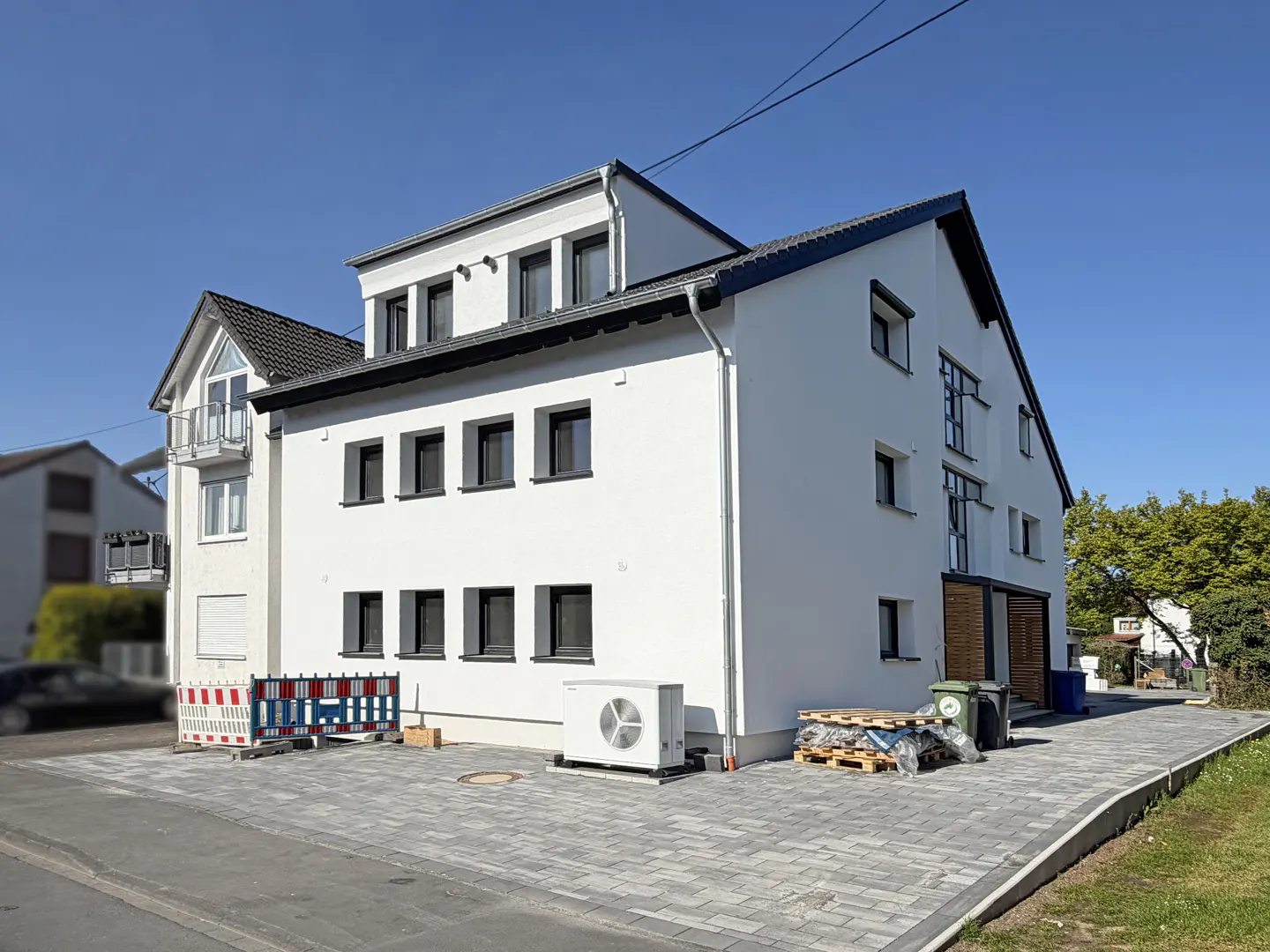 Exterior view of a modern, three-story white house with black window frames and a gray roof on a sunny day.