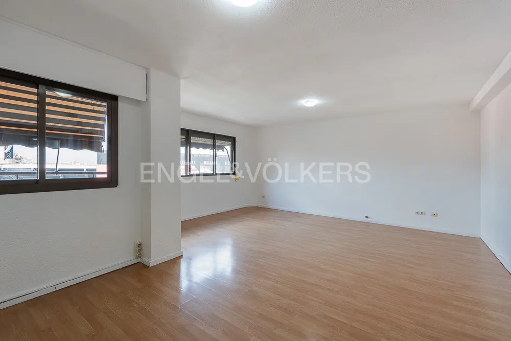 Bright, empty room with wood floors, white walls, and two windows with brown frames and blinds.