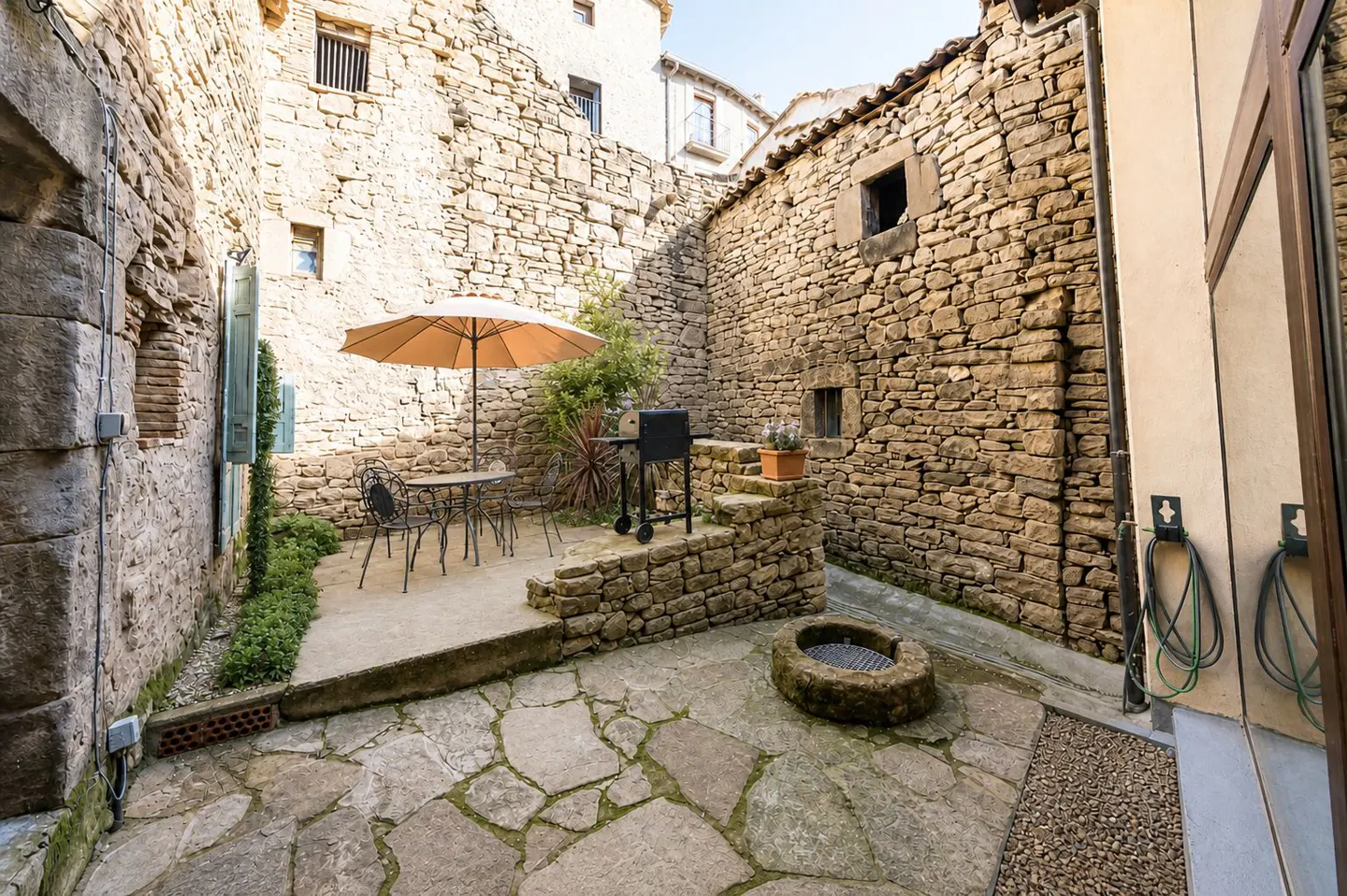 Stone courtyard with table, chairs, umbrella, and grill. Stone walls surround the outdoor space.