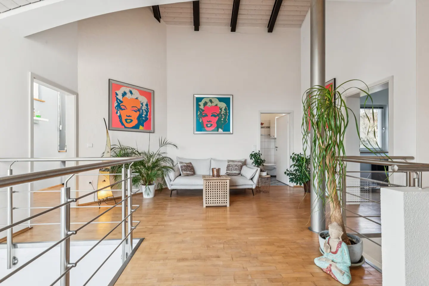 Bright, modern loft with wood floors, white walls, and high ceilings. Features Warhol-style art, a white sofa, and indoor plants.