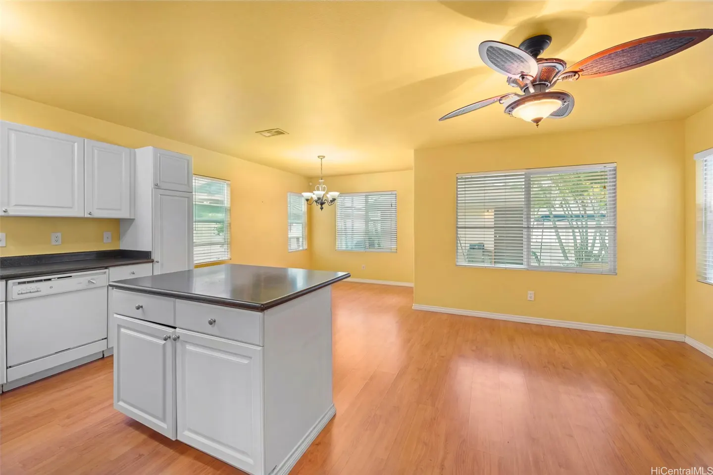 Bright yellow kitchen and dining area with white cabinets, island, and wood floors. A ceiling fan hangs above.