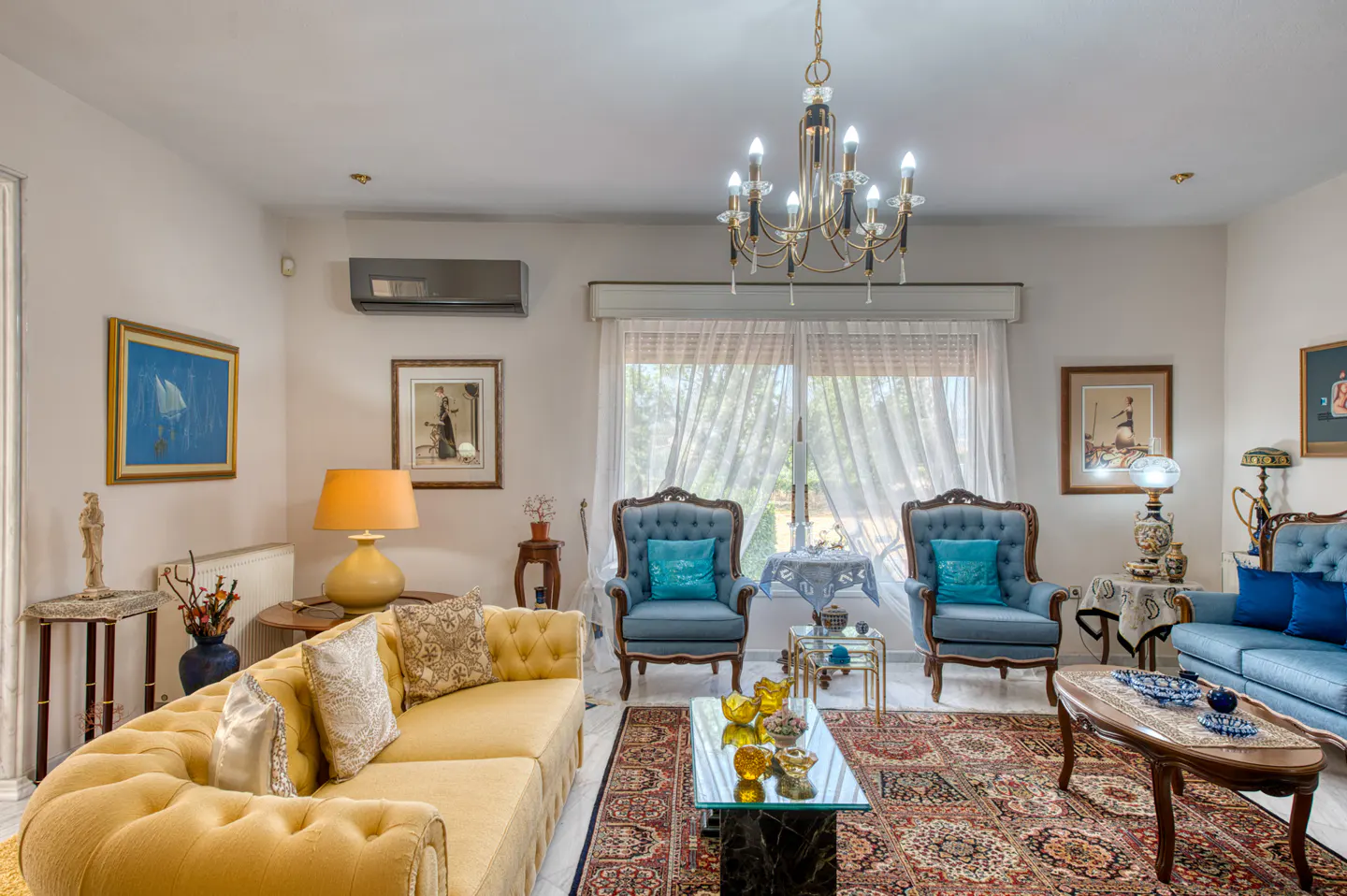 Bright living room with yellow sofa, blue chairs, patterned rug, and chandelier.