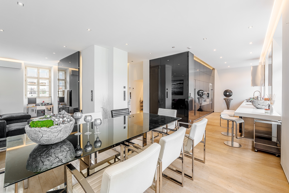 Modern dining area with a glass table, white chairs, and a sleek kitchen with bar stools on light wood floors. [AI-generated text]