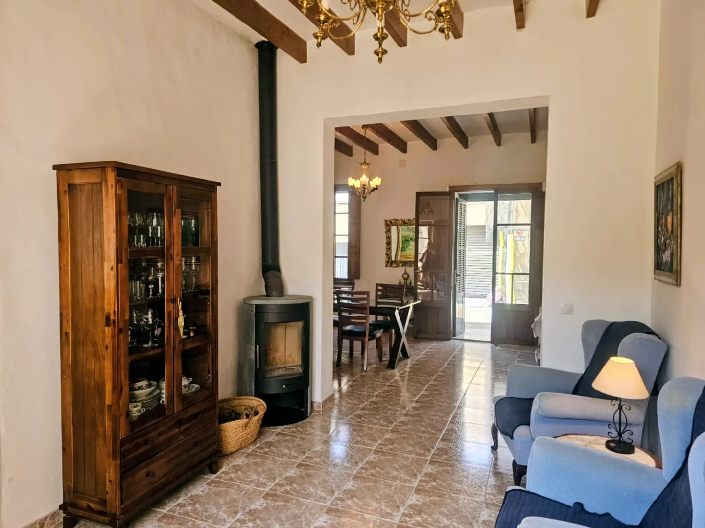 Living room with tile floors, wood cabinet, and fireplace. Dining room visible through doorway. Two blue armchairs in foreground.