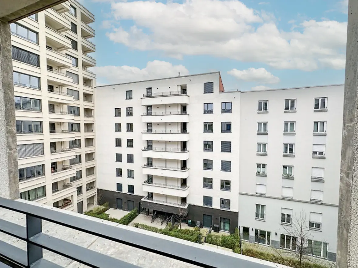 View from a balcony of two modern, white apartment buildings under a cloudy sky.