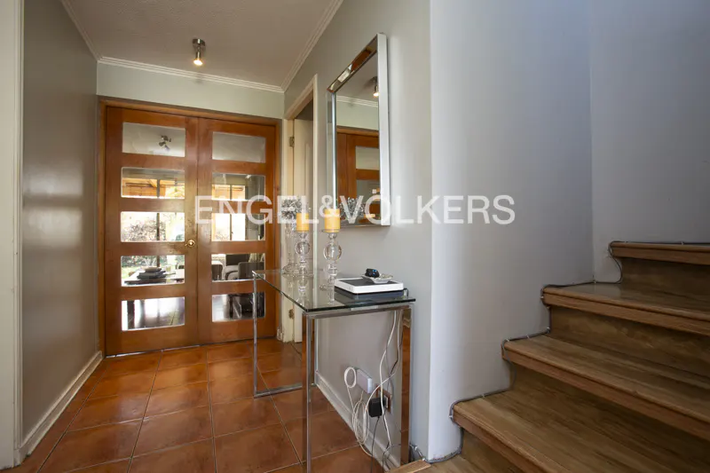Entryway with terracotta tile floor, glass console table, wall mirror, and wooden staircase leading to the upper level.