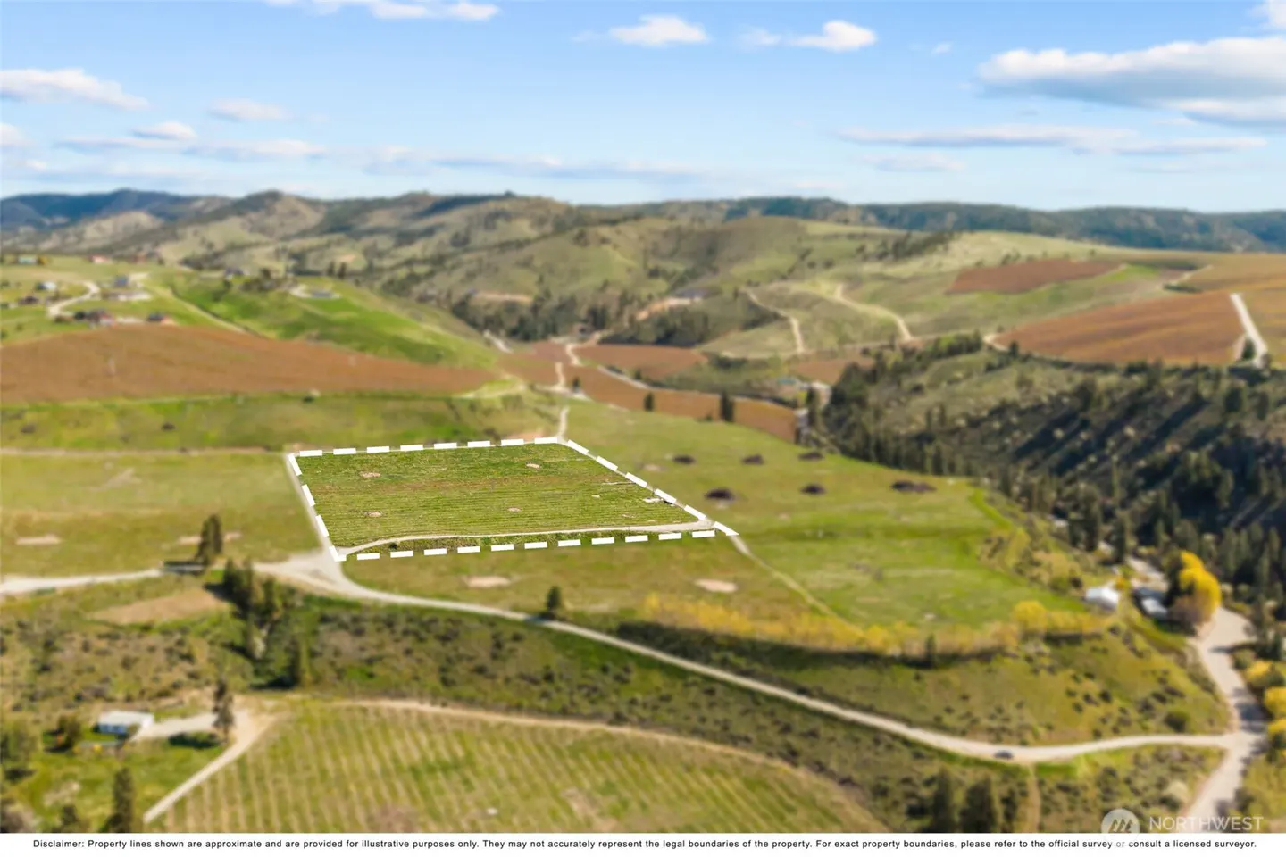 Aerial view of a green property lot outlined in white, set against a backdrop of rolling hills and a blue sky.