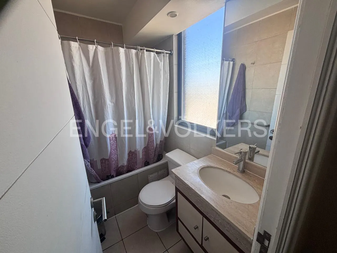 Bathroom with a white shower curtain with a city skyline design, toilet, and vanity with a marble countertop.