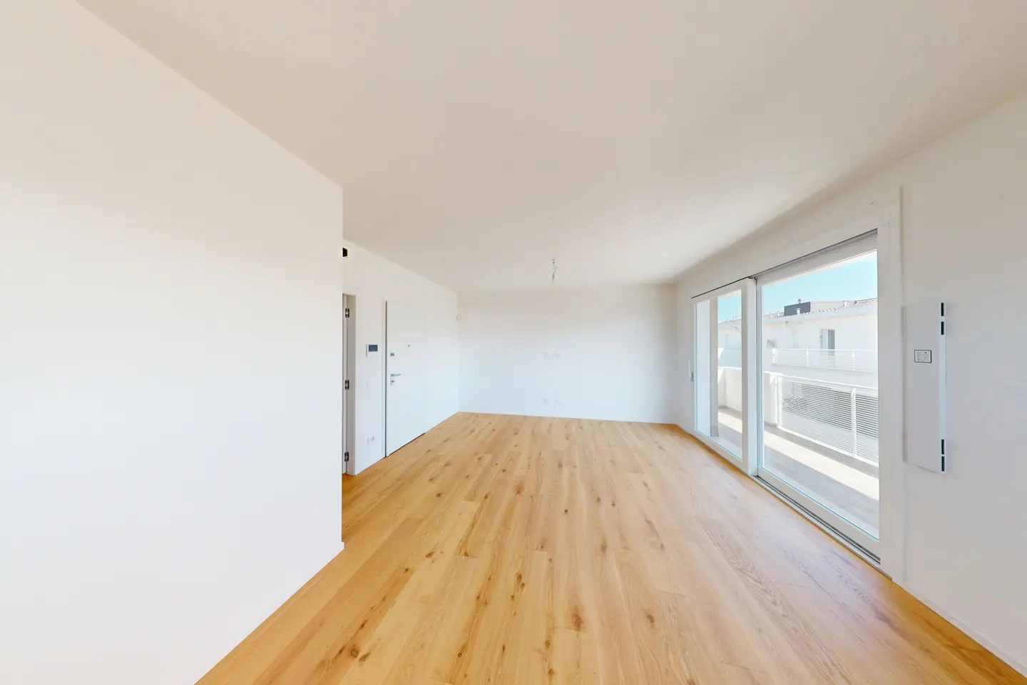 Bright, empty room with light wood floors, white walls, and sliding glass doors to a balcony.