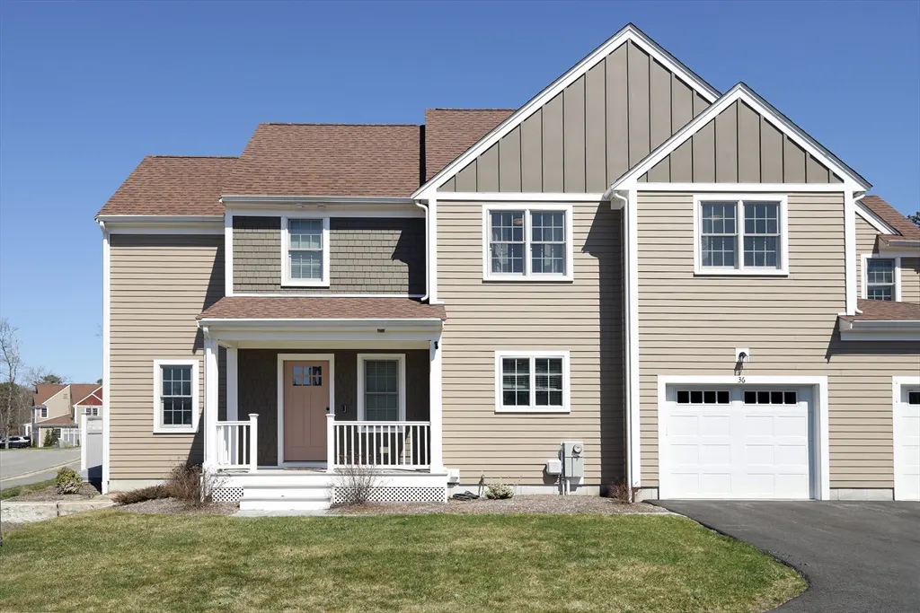 Tan two-story townhouse with a brown roof, white trim, and a white garage door under a clear blue sky.