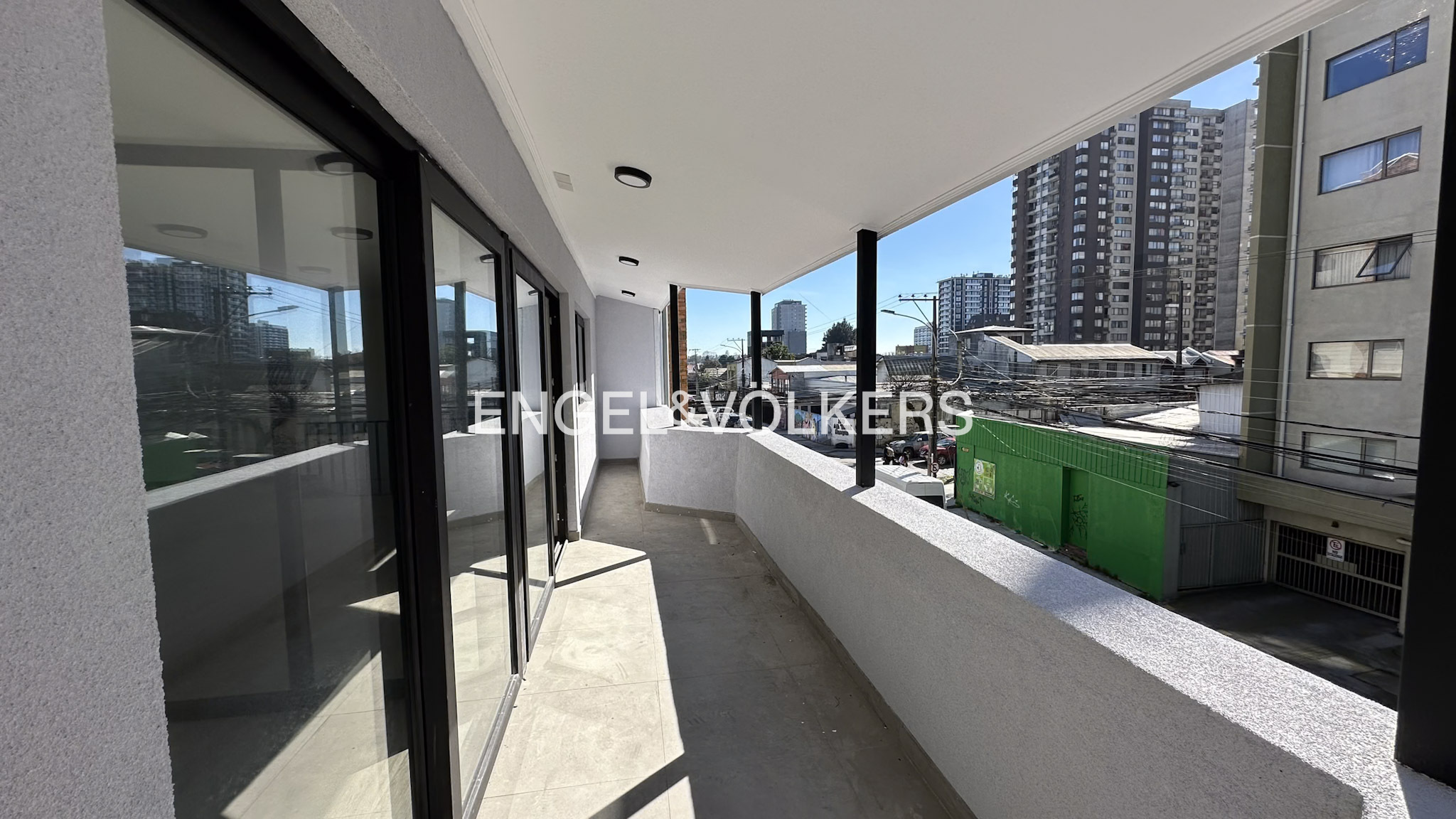 Modern apartment balcony with glass sliding doors, white walls, and a view of surrounding city buildings and streets. [AI-generated text]
