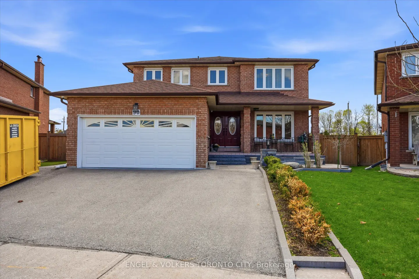 Two-story brick house with a white garage door, brown roof, and a green lawn under a blue sky.