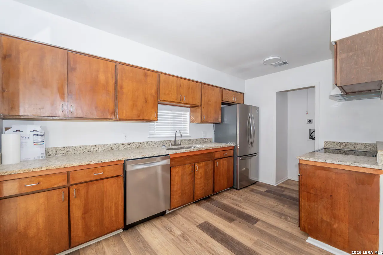 A kitchen with wood cabinets, stainless steel appliances, granite countertops, and wood-look flooring.