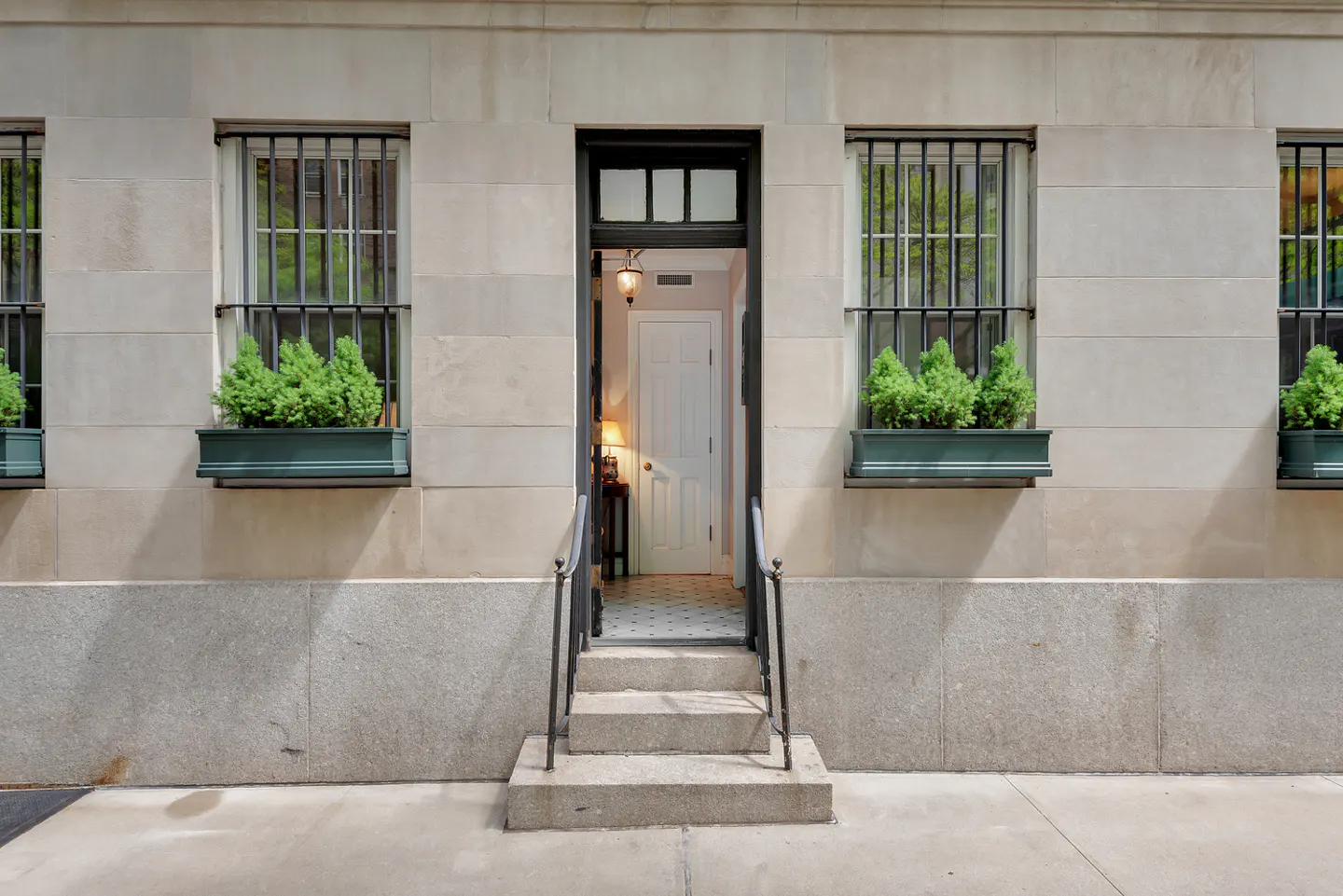 Exterior of a stone building with a black door, steps, and window boxes with greenery.
