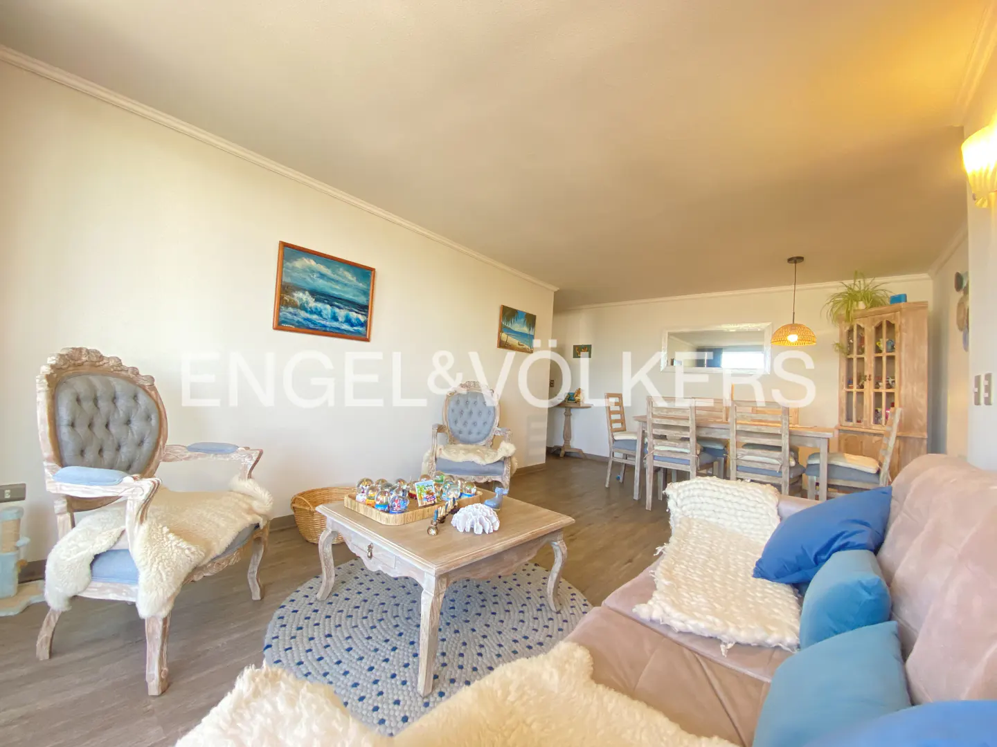 Living room with blue and white accents, featuring a sofa, chairs, a coffee table, and a dining area in the background.