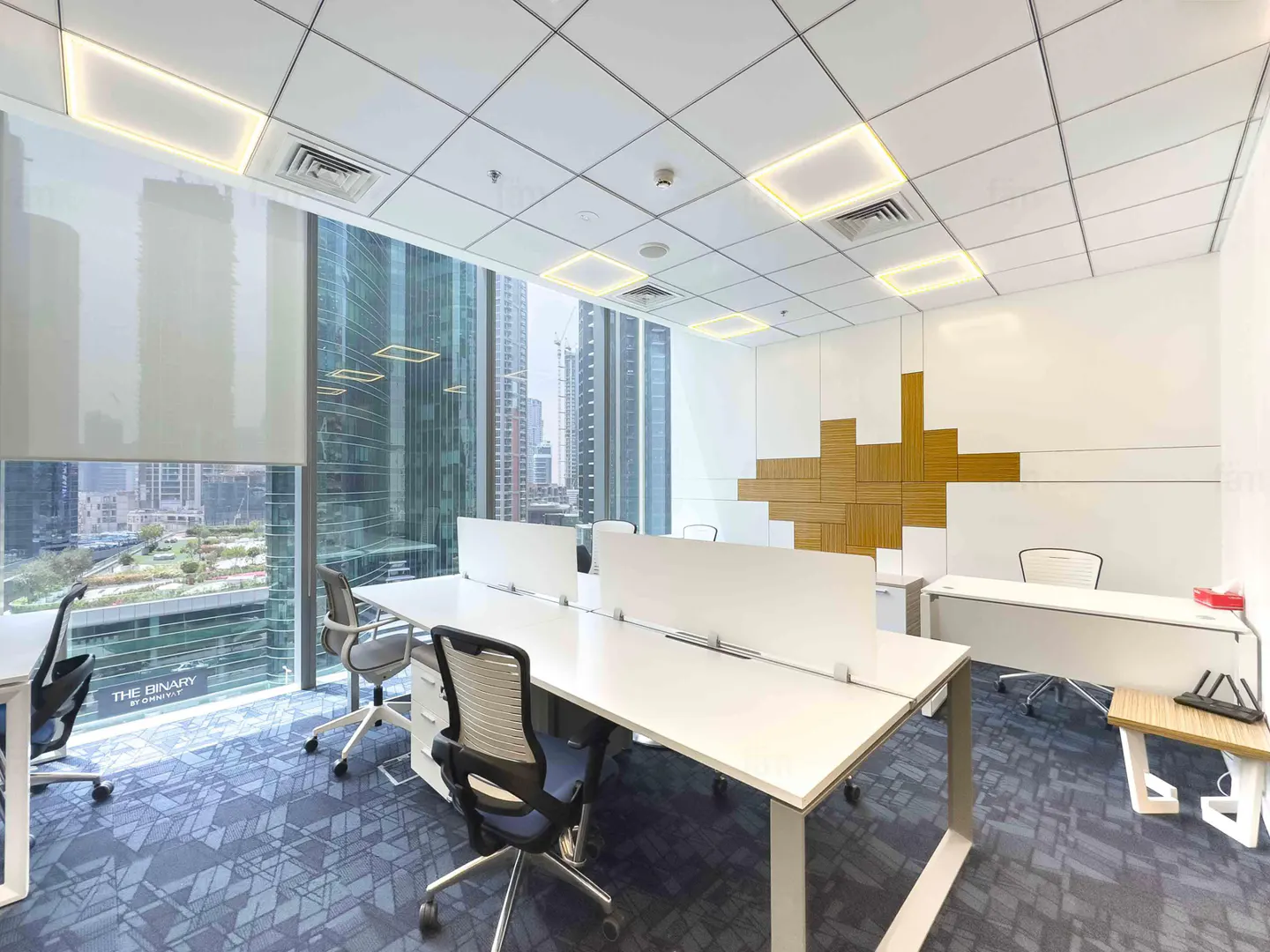 Bright office space with white desks, blue chairs, and a large window overlooking city buildings.