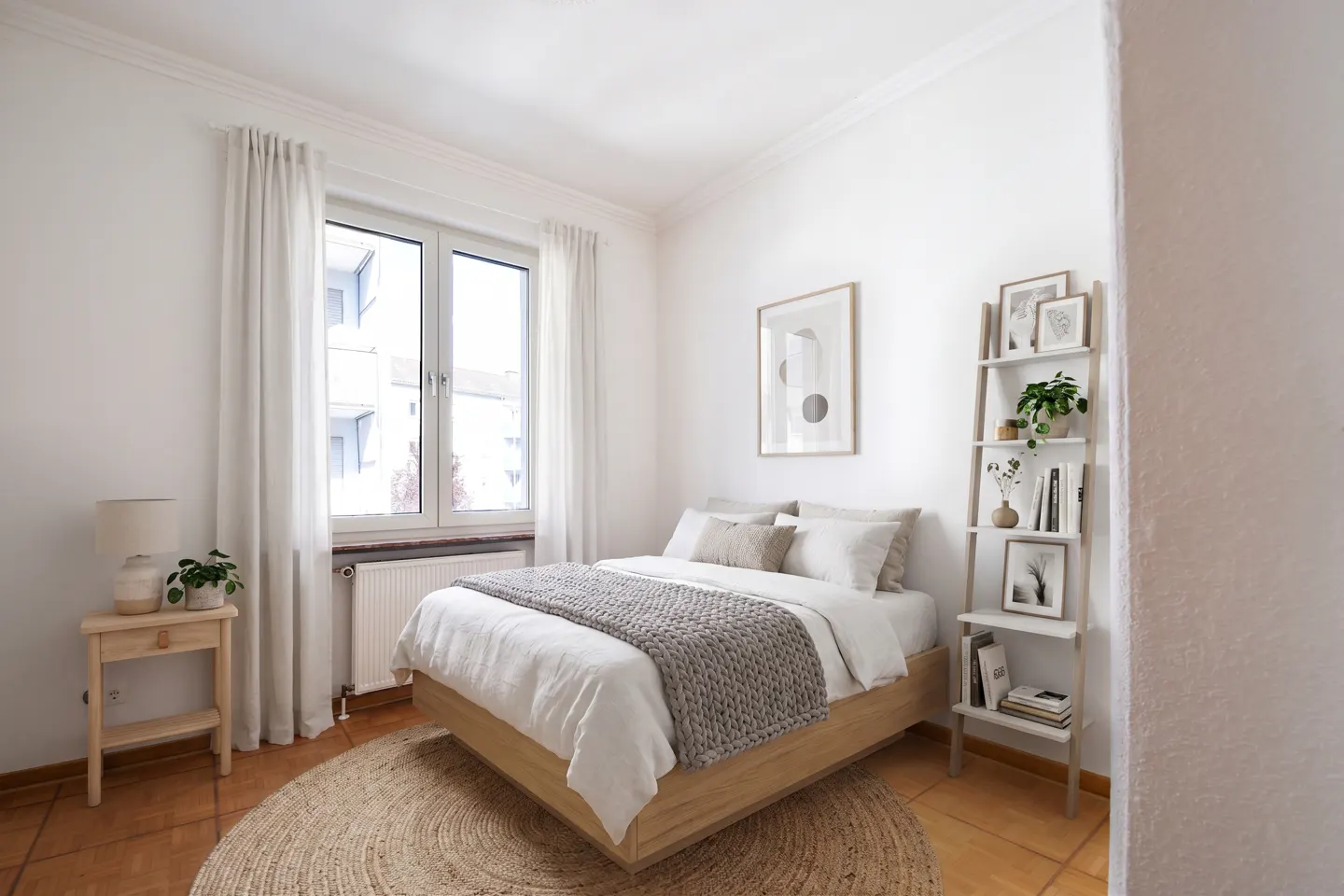 Bright bedroom with white walls, a wooden bed frame, and a gray knit blanket. A ladder shelf holds books and plants.