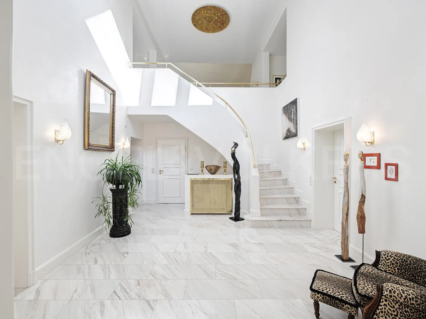 Grand white foyer with marble floors, a sweeping staircase with gold railing, modern art, and a leopard-print armchair.