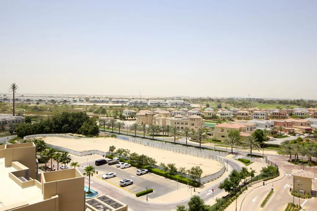 An aerial view of a residential area with beige buildings, palm trees, and parked cars under a hazy sky.