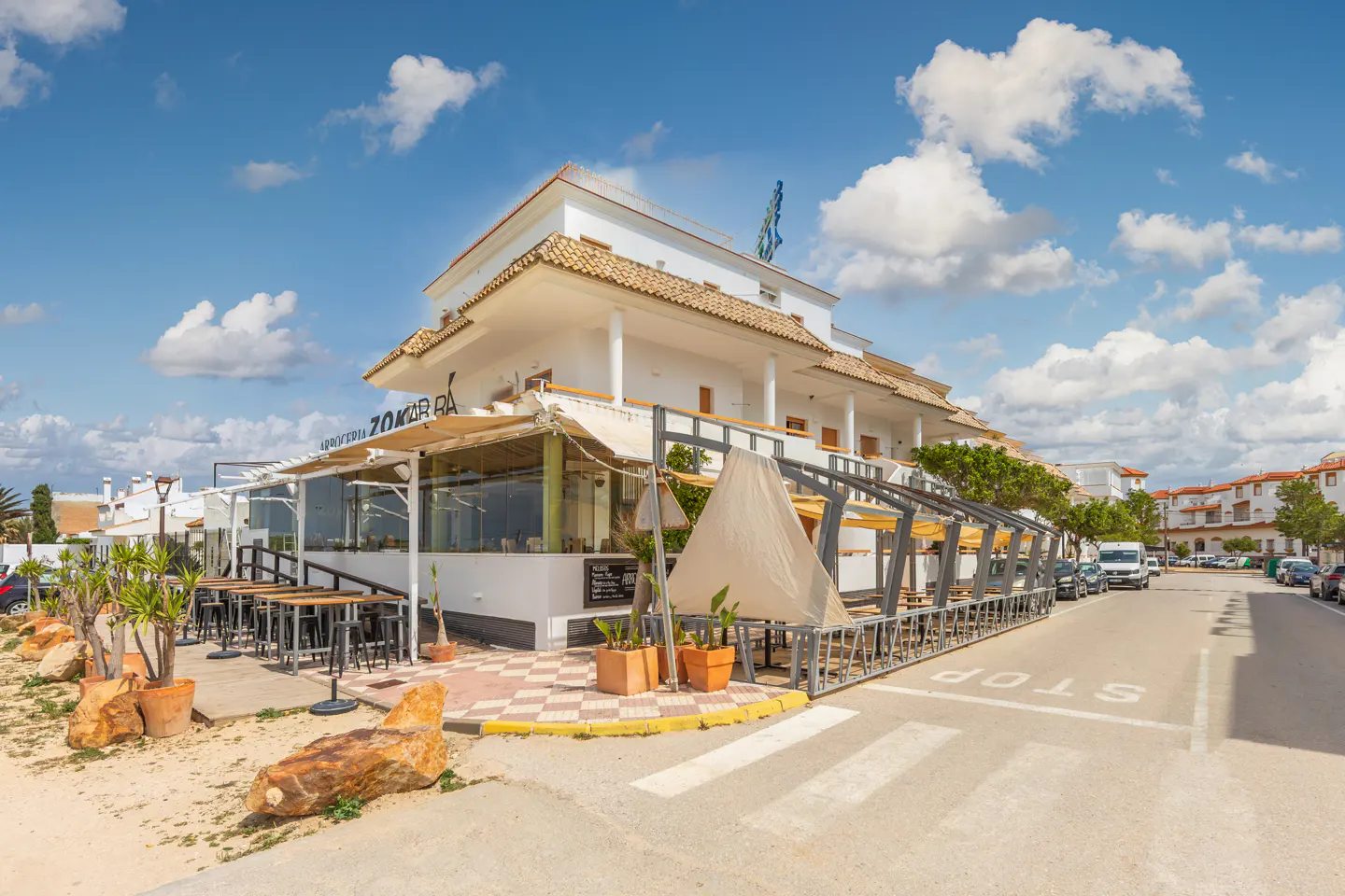 Exterior view of a white, two-story restaurant with outdoor seating under a canopy, located on a street with parked cars.