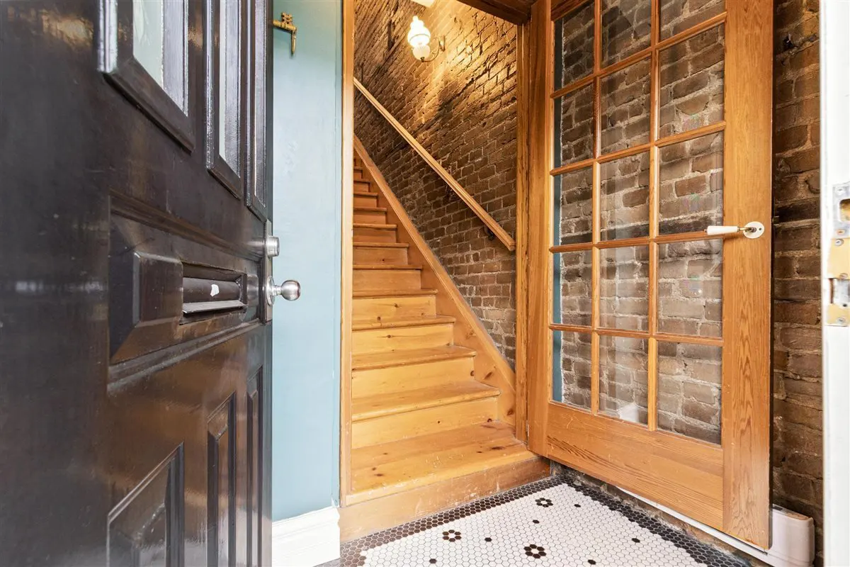 Open front door reveals a staircase with brick walls and a glass paneled door. The floor has a black and white tile pattern.