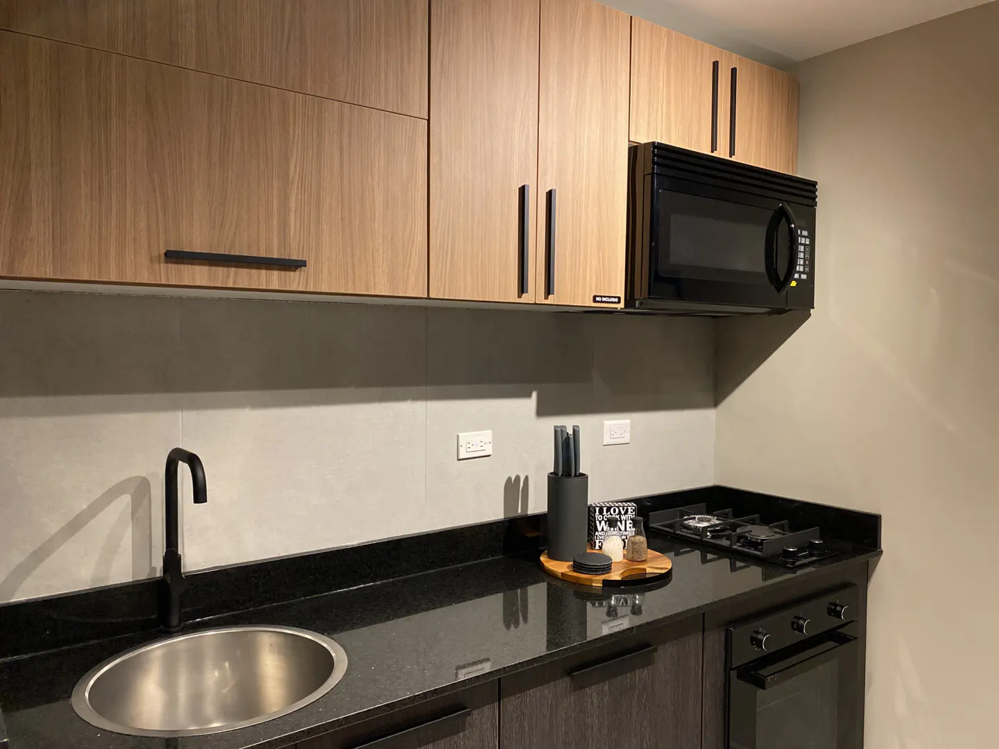 Modern kitchen with wood-grain upper cabinets, black countertops, a stainless steel sink, and a built-in microwave.