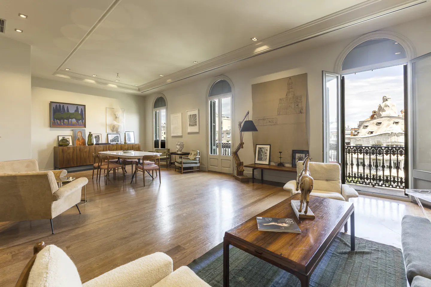 Bright, airy living room with hardwood floors, neutral furniture, and art. Balcony doors open to a city view.