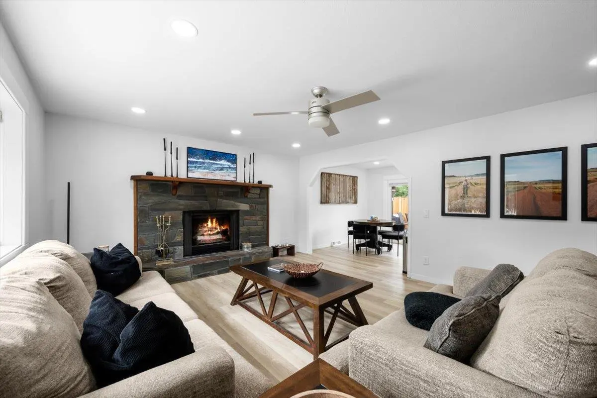 Bright living room with a stone fireplace, tan sofas, and a dark wood coffee table. Three framed photos hang on the wall.