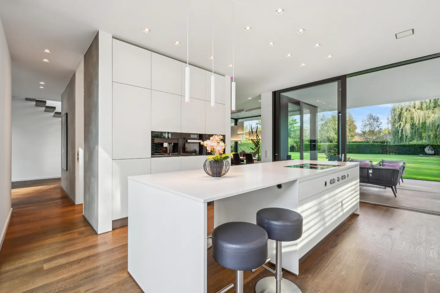 Bright, modern kitchen with white cabinets, island with stools, and large sliding glass doors to a green lawn.