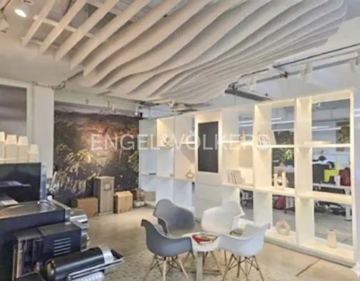 Engel & Völkers office space with a modern, wavy white ceiling. Gray chairs surround a small table. White shelving units divide the space.