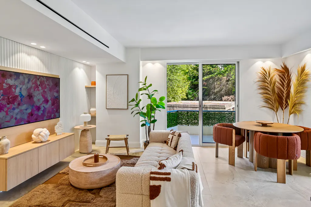 Bright, modern living room with a cream sofa, round wood table, and rust-colored chairs near a sliding glass door to a green outdoor space.