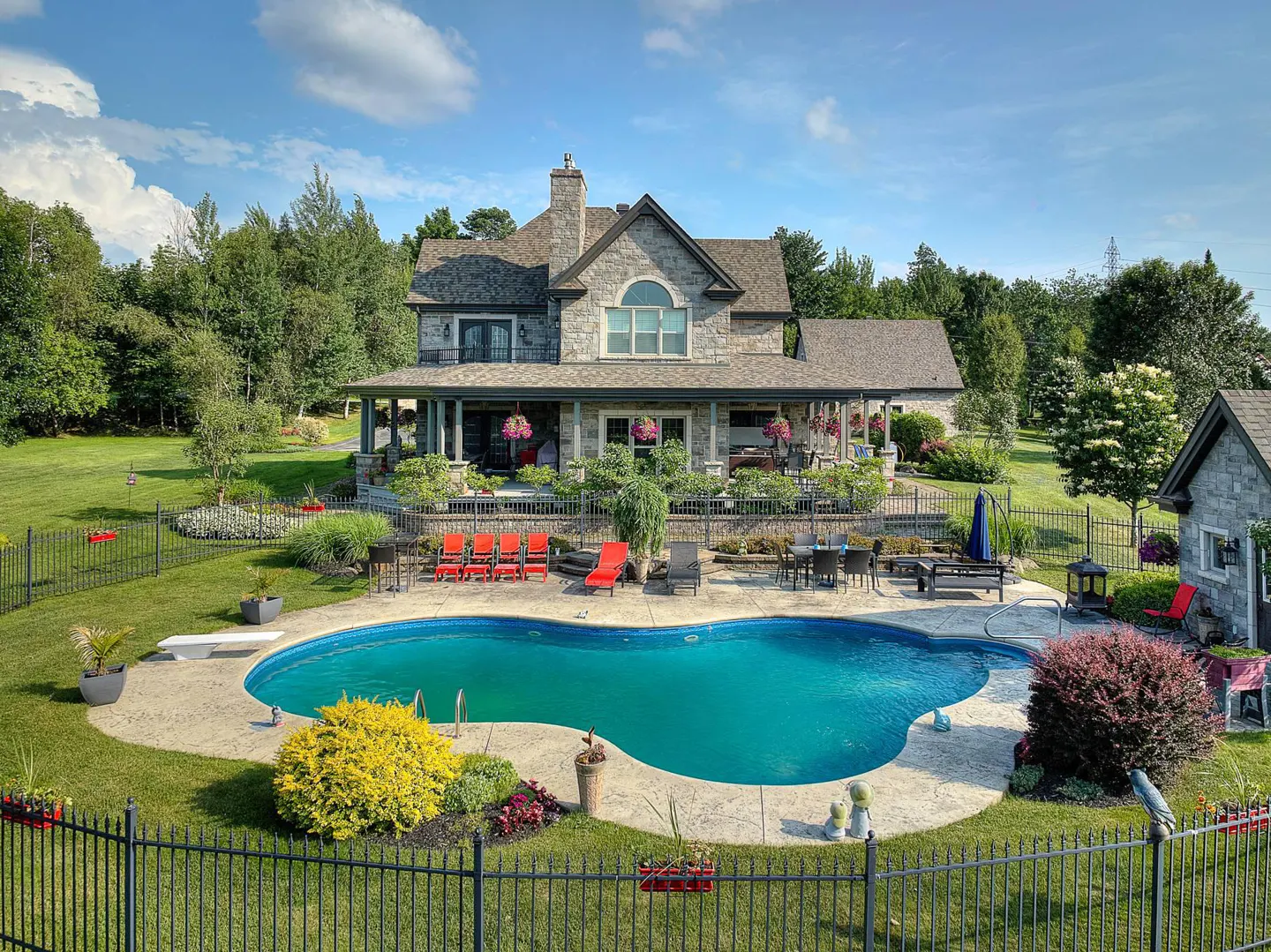 A large stone house with a pool and a green lawn on a sunny day.