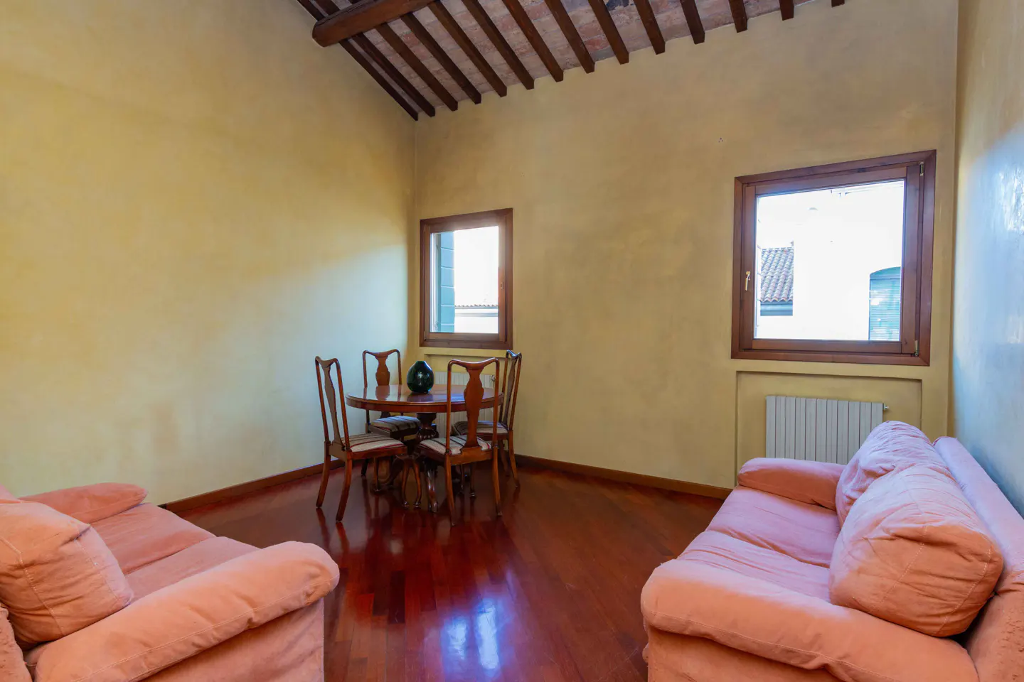 Living room with yellow walls, wood floors, exposed beam ceiling, pink sofas, and a round table with four chairs.