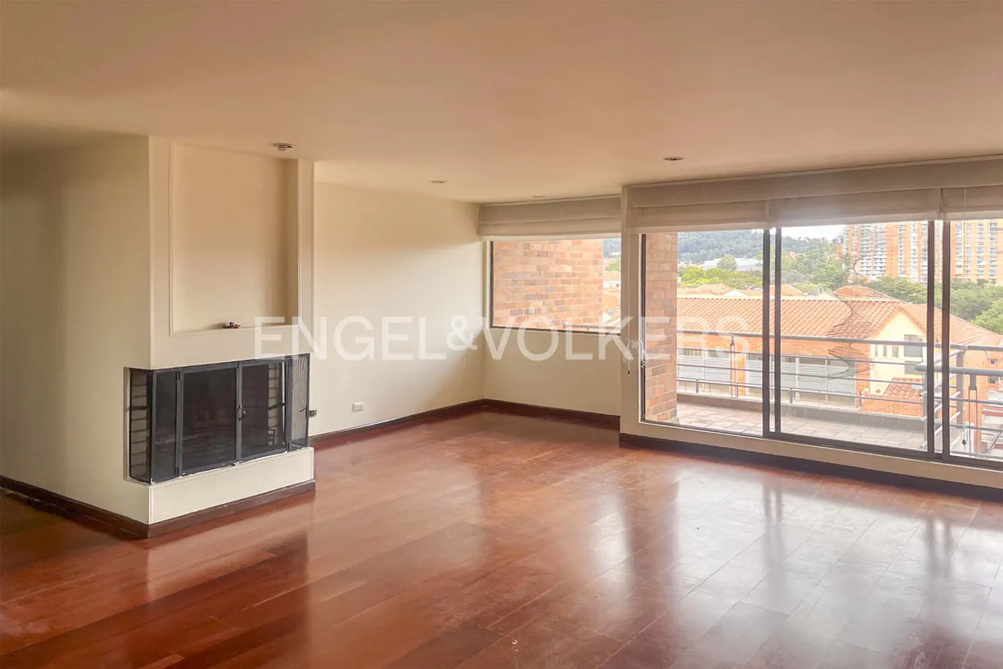 Bright living room with hardwood floors, a fireplace, and large windows overlooking a cityscape.