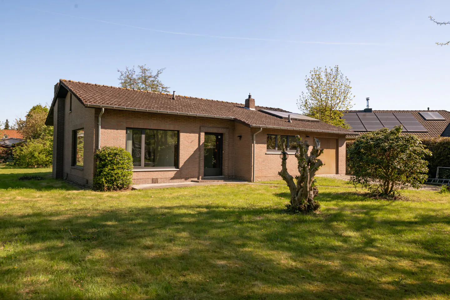A single-story brick house with a brown roof and green lawn on a sunny day.