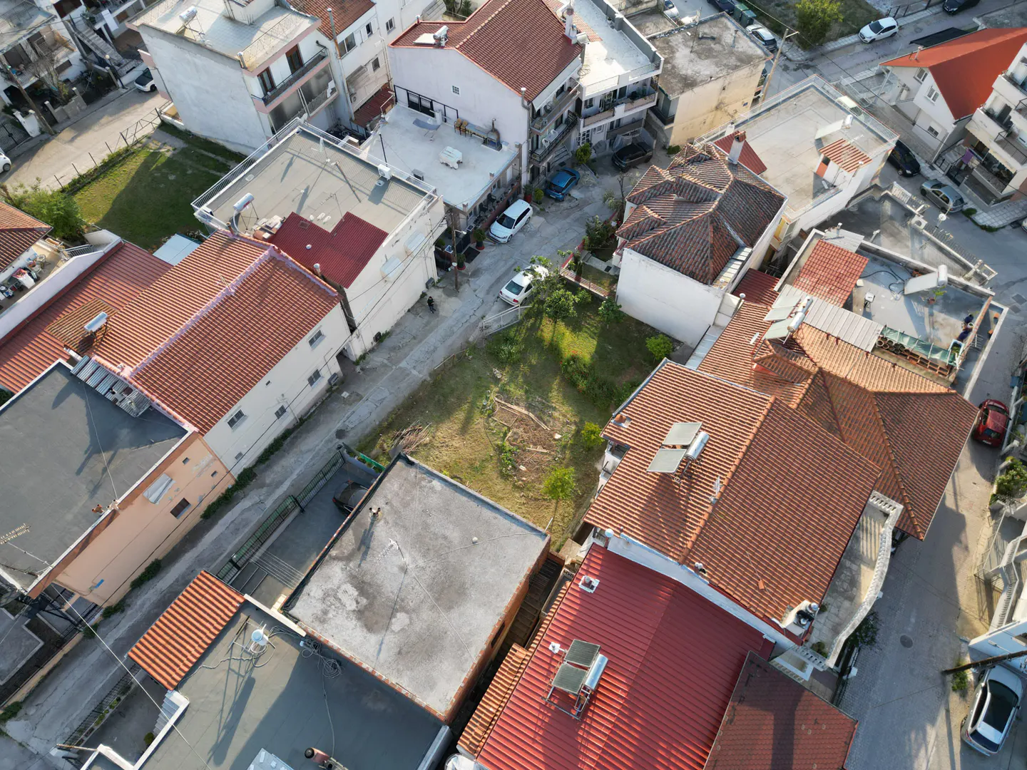 Aerial view of a neighborhood with houses with red tile roofs and a grassy lot.