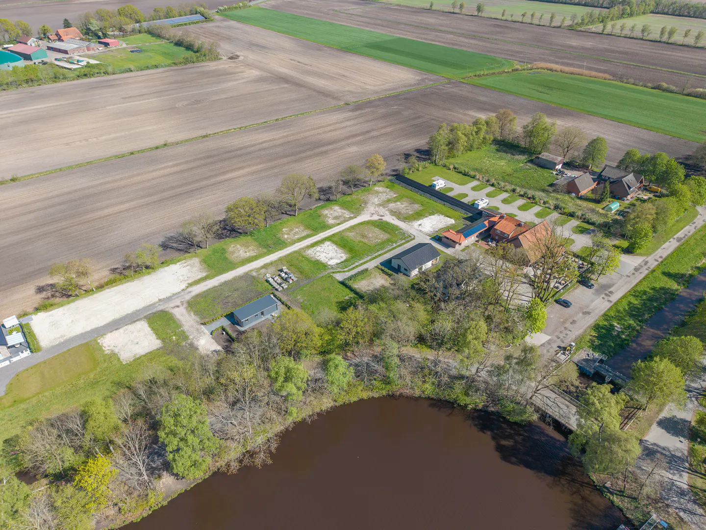 Aerial view of a property with a lake, fields, and buildings. The property includes a campground, houses, and green spaces.