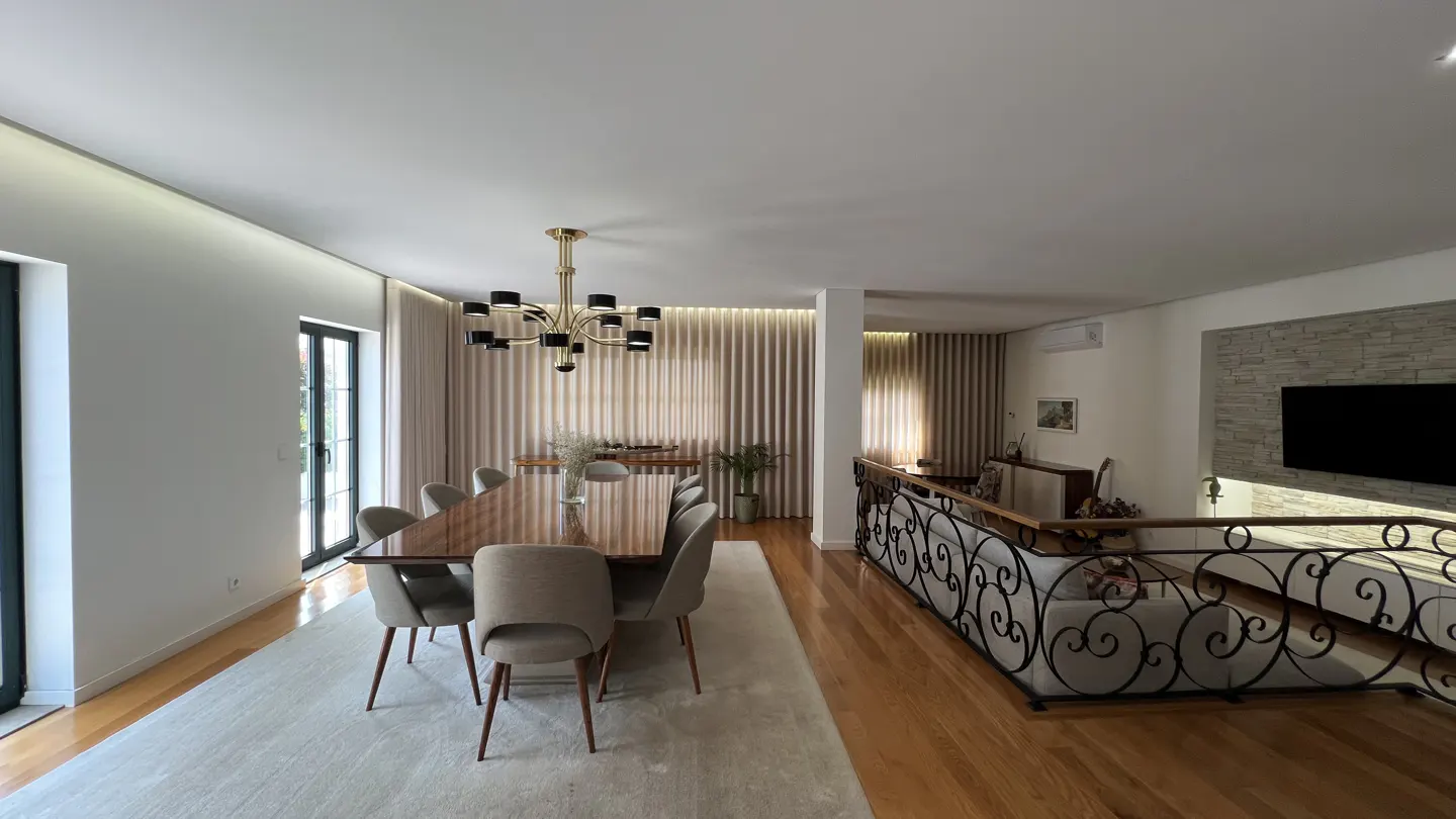Open-concept dining and living room with wood floors, a long dining table with chairs, and a wrought iron railing overlooking the living area.