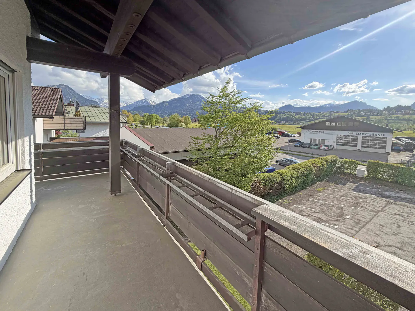 View from a balcony with brown wooden railings, overlooking a garage and mountains under a blue sky.