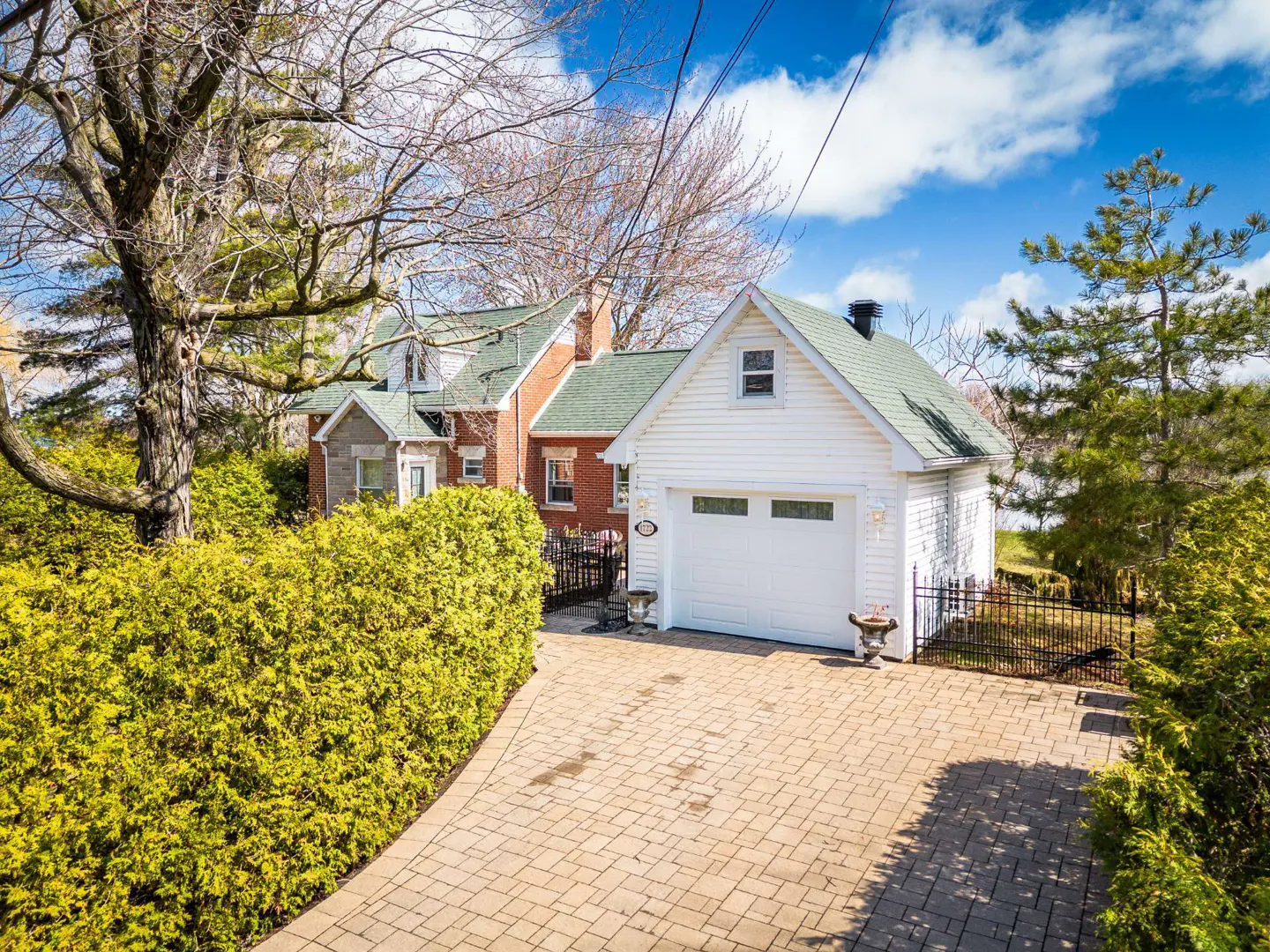 Exterior view of a house with a white garage, brick house, green roof, and a brick driveway.