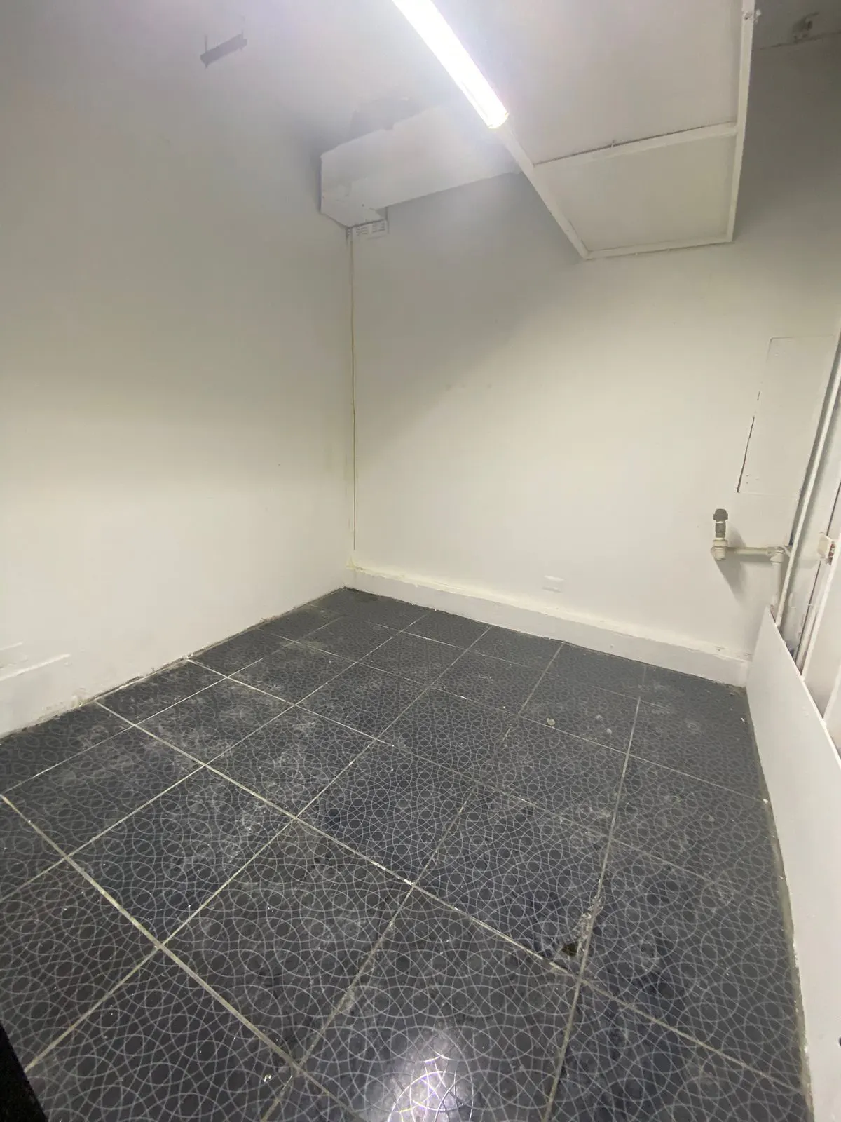 Empty room with white walls, black patterned tile floor, and a fluorescent ceiling light.