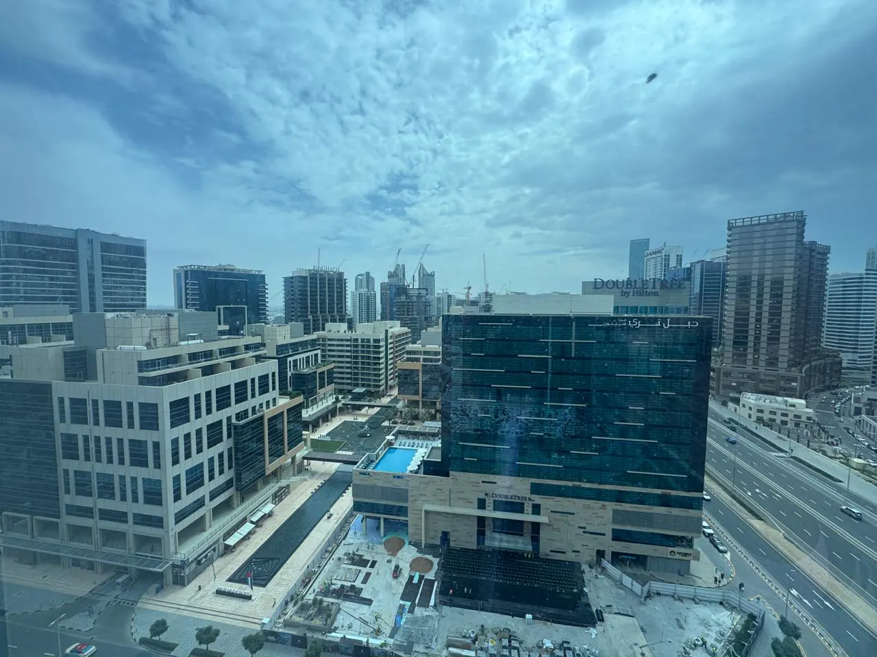 High-angle view of a modern city skyline with a DoubleTree by Hilton hotel, a rooftop pool, and a multi-lane highway.