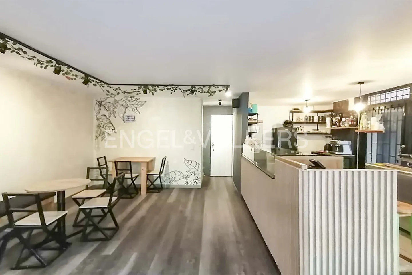 Interior view of a cafe with tables, chairs, and a counter. Walls are decorated with plant motifs.
