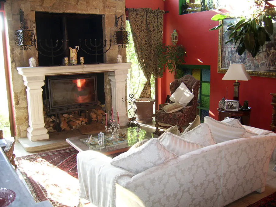 Cozy living room with a stone fireplace, white sofa, patterned armchair, and red walls. A glass coffee table sits in front of the sofa.