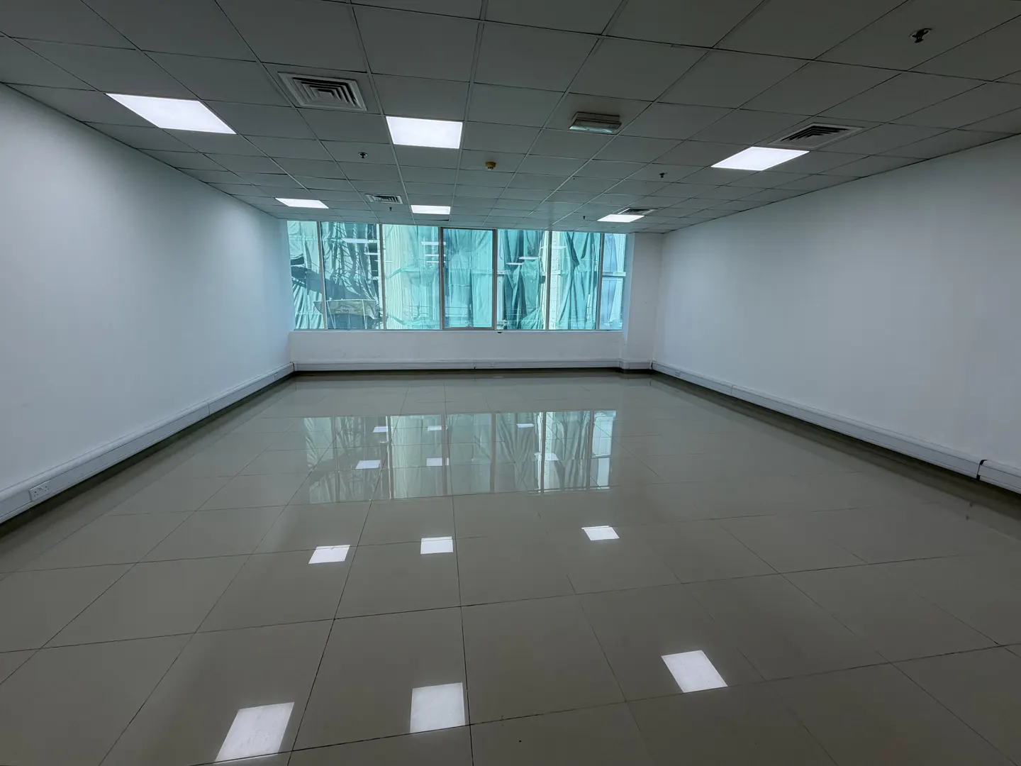 Empty office space with white walls, tile floor, and a window covered with green tarp.