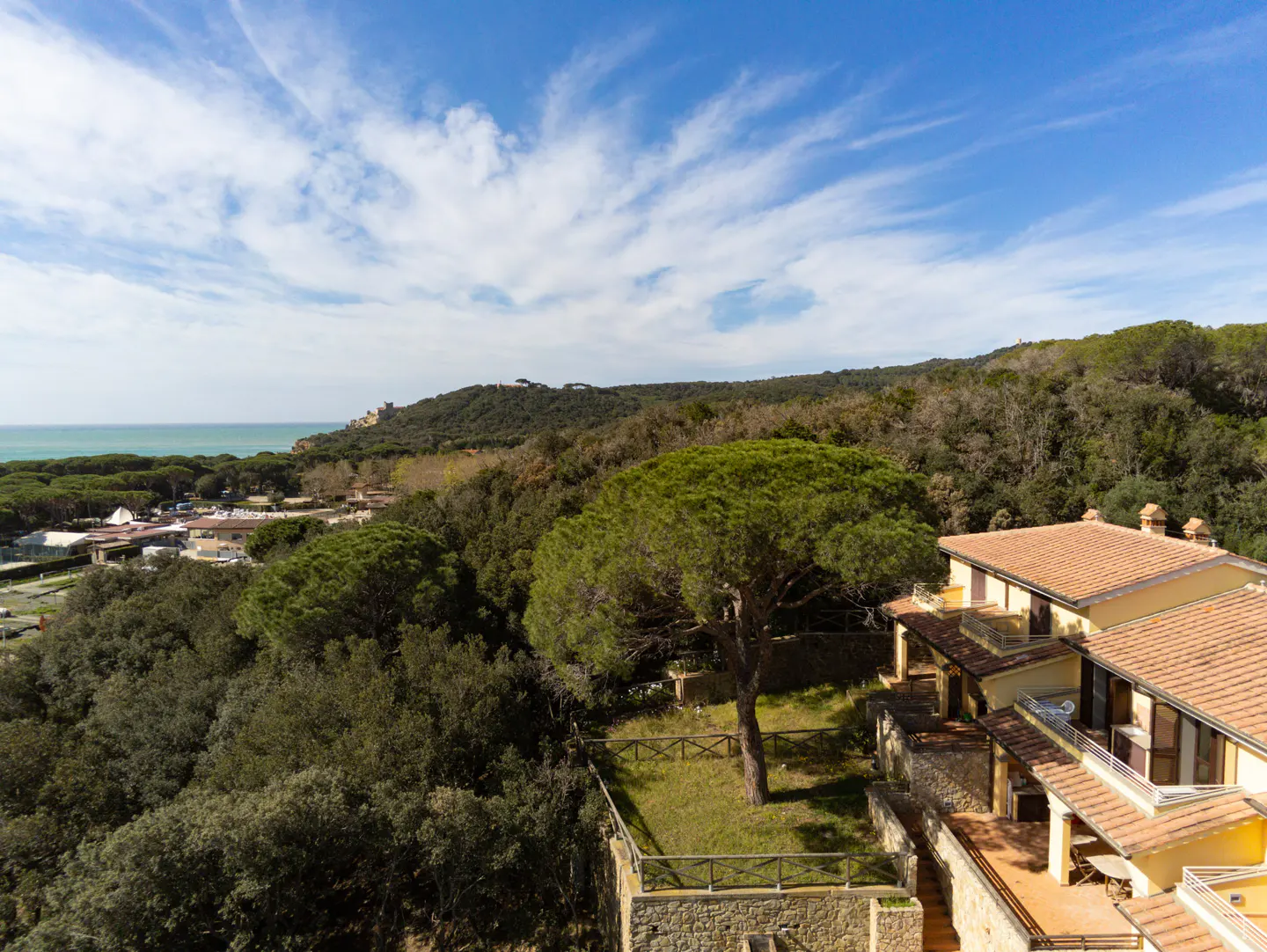 Scenic view of a yellow building with a red tile roof, surrounded by green trees and a blue sky with white clouds.