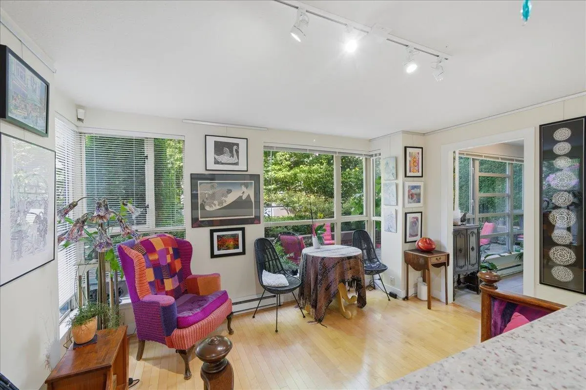 Bright living area with hardwood floors, a colorful patchwork armchair, a small round table, and walls filled with art.