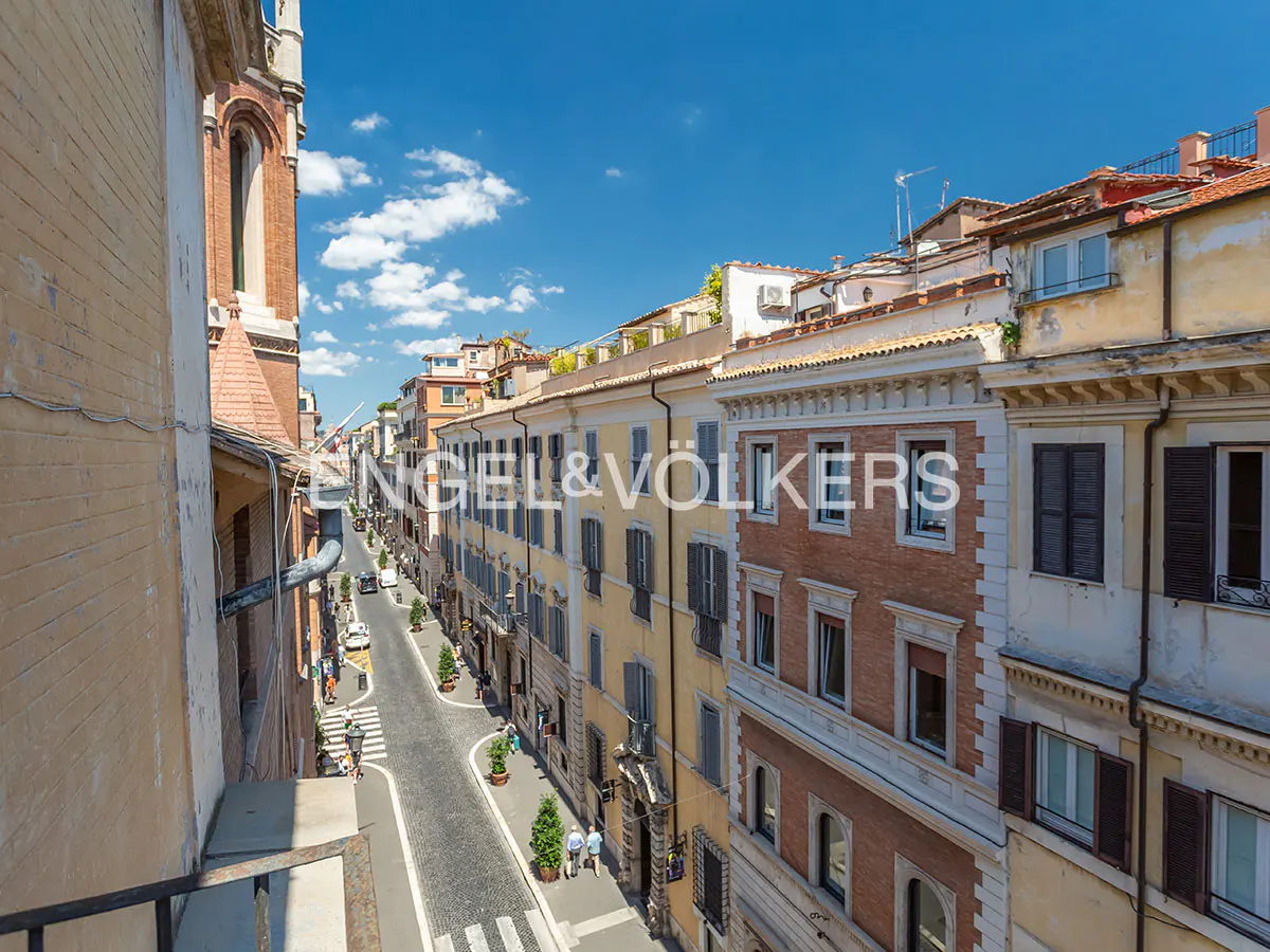 High-angle view of a narrow, cobblestone street in Rome lined with historic yellow and brick buildings under a blue sky.