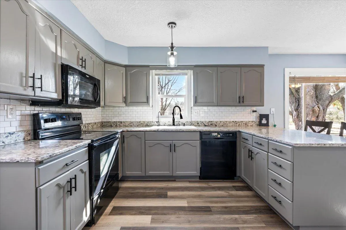 A modern kitchen with gray cabinets, black appliances, granite countertops, and wood-look flooring.
