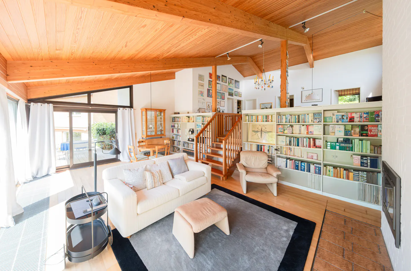 Bright living room with wood ceiling, white sofa, and floor-to-ceiling bookshelves. Stairs lead to a second level.